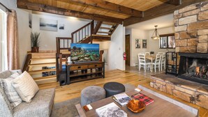 A spacious living area with a wooden staircase, a fireplace, and a television on a wooden entertainment unit.