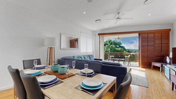Ein modernes Wohnzimmer mit Essbereich, einer Couch, einem Deckenventilator und einem Balkon mit Blick.