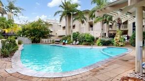 Ein Pool mit geschwungener Kante, umgeben von Palmen und einem Gebäude mit Balkonen.