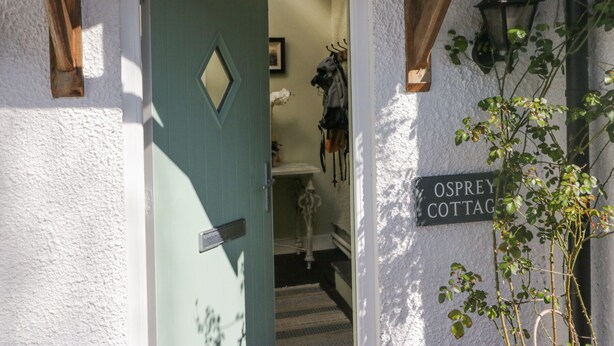 A doorway to Osprey Cottage with a green door and a sign on the wall.