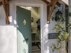 A doorway to Osprey Cottage with a green door and a sign on the wall. - Osprey Cottage (Ambleside)