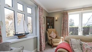 A cozy living room with a large window, a wooden chair, a sofa, and a decorative sailboat model on the windowsill.