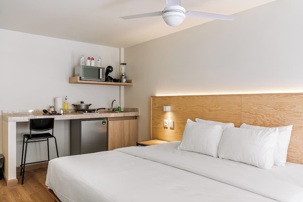 A hotel room with a bed, a desk with a microwave, a refrigerator, and a chair.