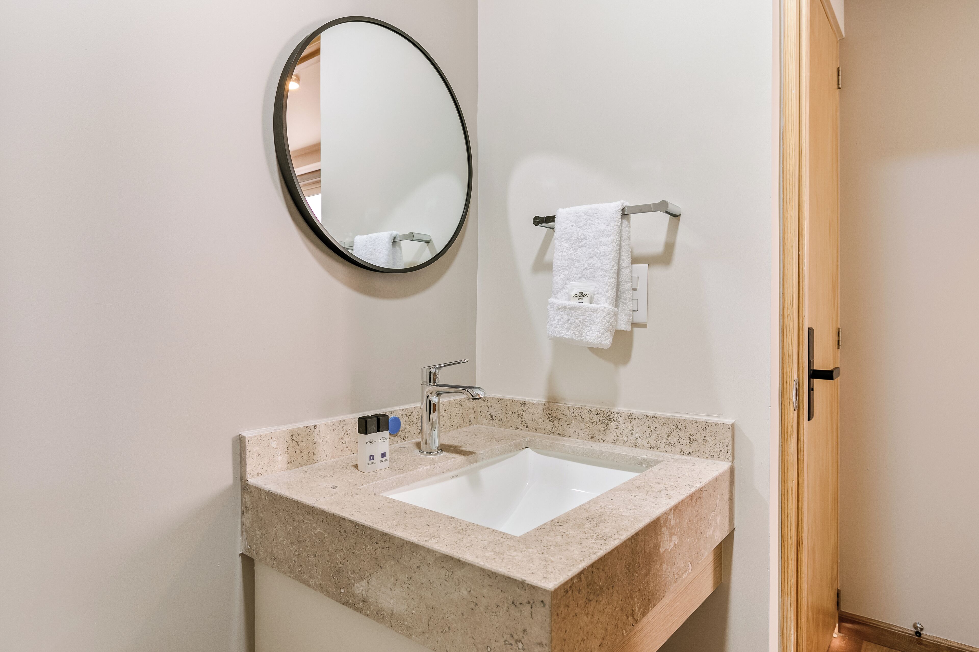 A bathroom with a white sink, a round mirror, and a towel rack.