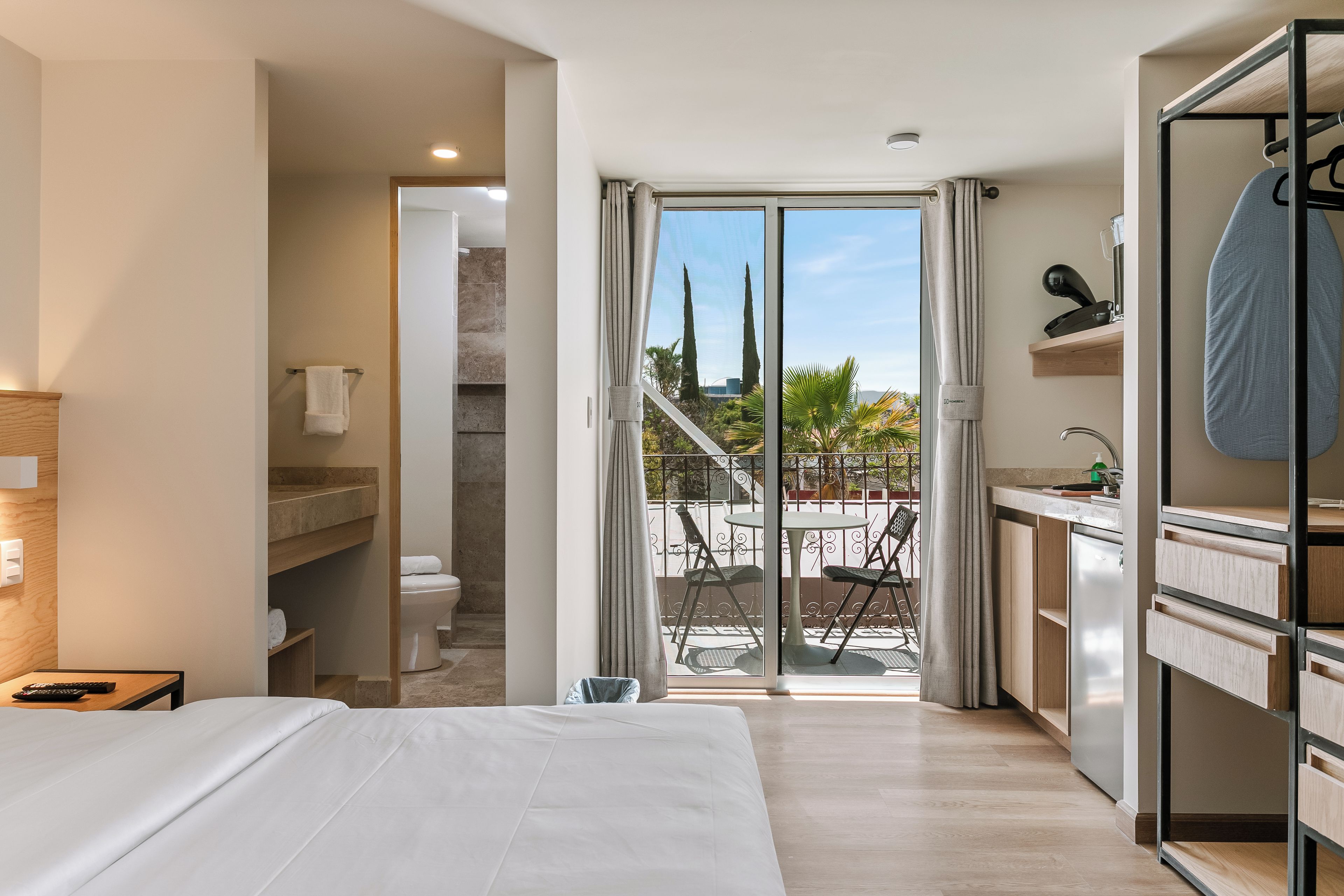 A hotel room with a bed, a bathroom, a balcony with a view, and a kitchenette.