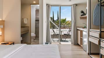 A hotel room with a bed, a bathroom, a balcony with a view, and a kitchenette.