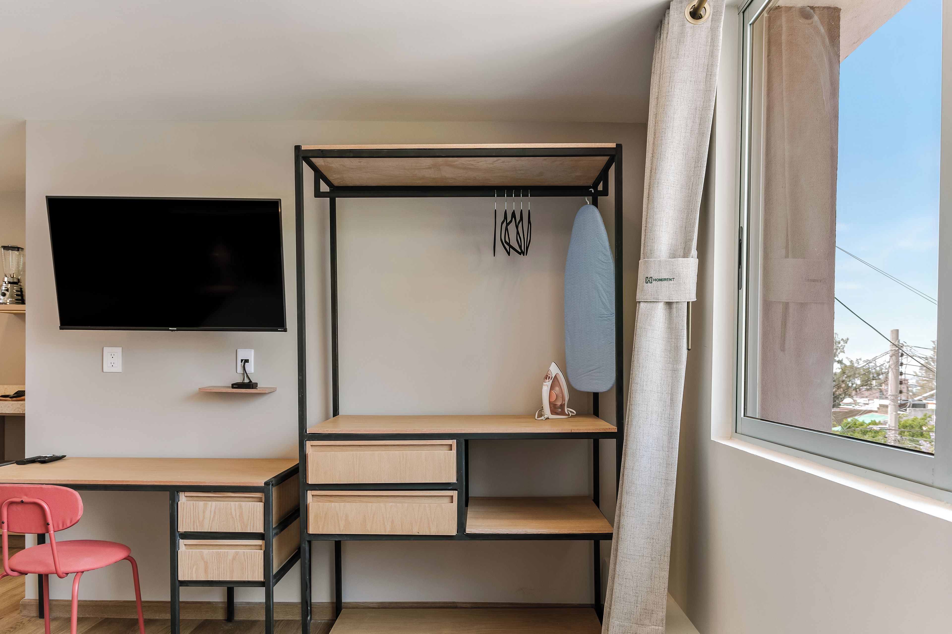 Une chambre à coucher de taille réduite, comprenant un lit, un bureau, une chaise, un téléviseur et une fenêtre avec des rideaux.
