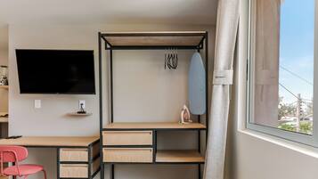Une chambre à coucher de taille réduite, comprenant un lit, un bureau, une chaise, un téléviseur et une fenêtre avec des rideaux.