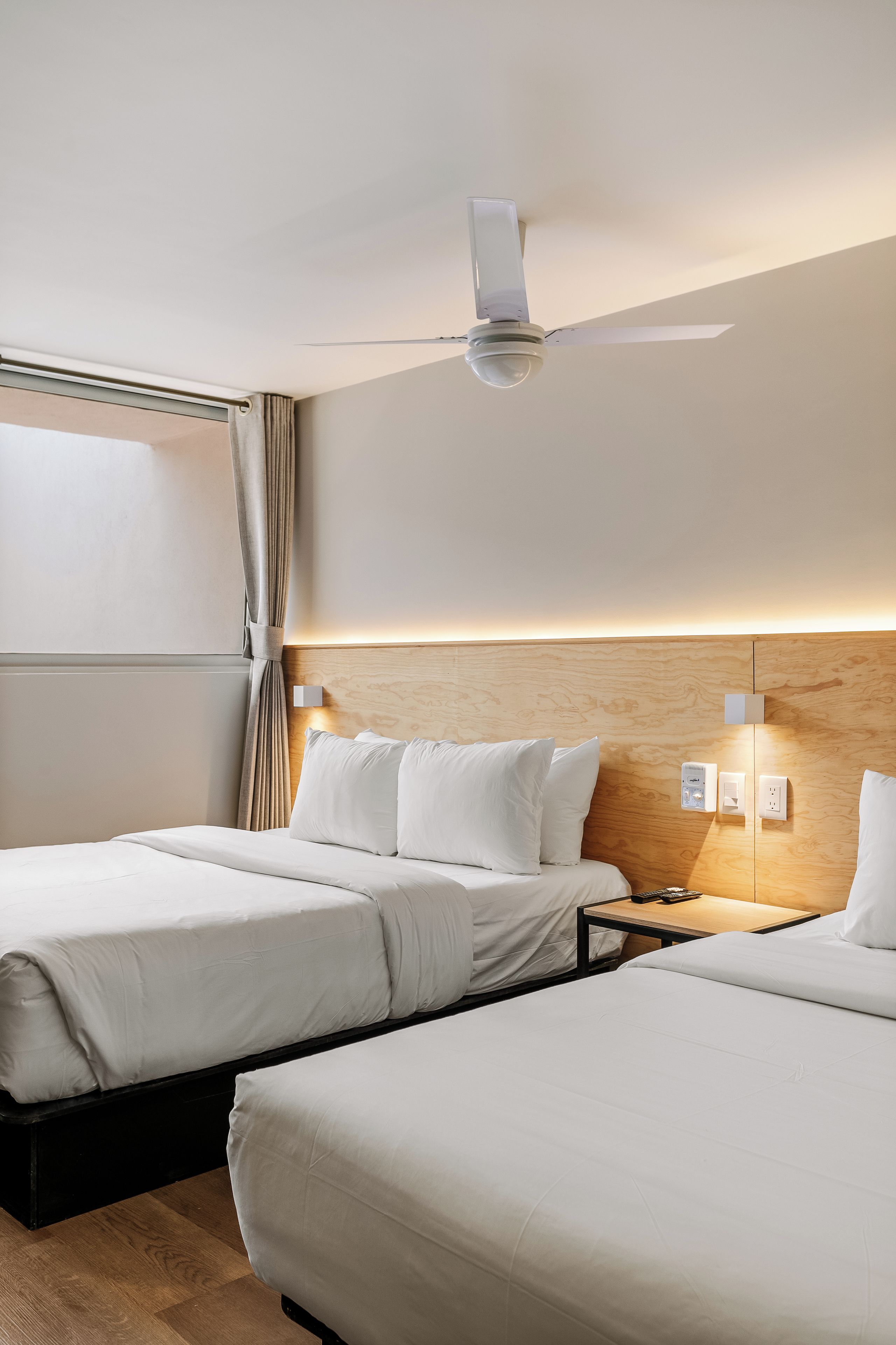 Ett hotellrum med två sängar, en takfläkt, ett nattduksbord med en lampa och en sänggavel i trä.