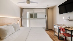 Una habitación de hotel con cama, escritorio y silla, televisor y ventana con cortinas.