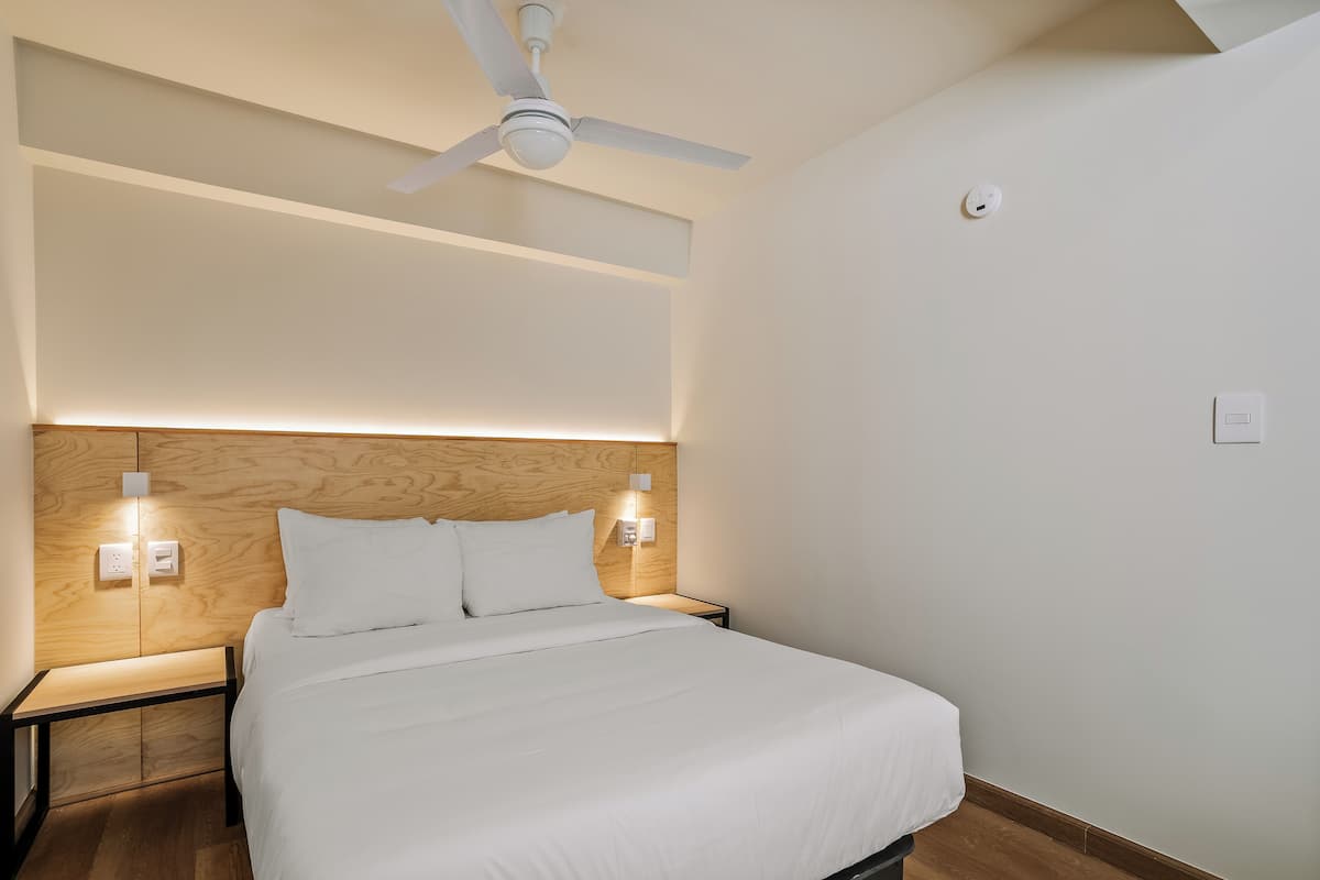 A modern hotel room with a wooden headboard, a single bed, bedside lamps, and a ceiling fan.