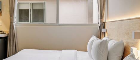 A hotel room with two beds, a ceiling fan, a window with curtains, and a nightstand with a lamp.