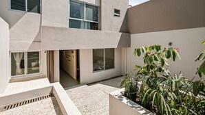 Un edificio moderno con numerosas ventanas, una entrada pequeña y un jardín con diversas plantas.