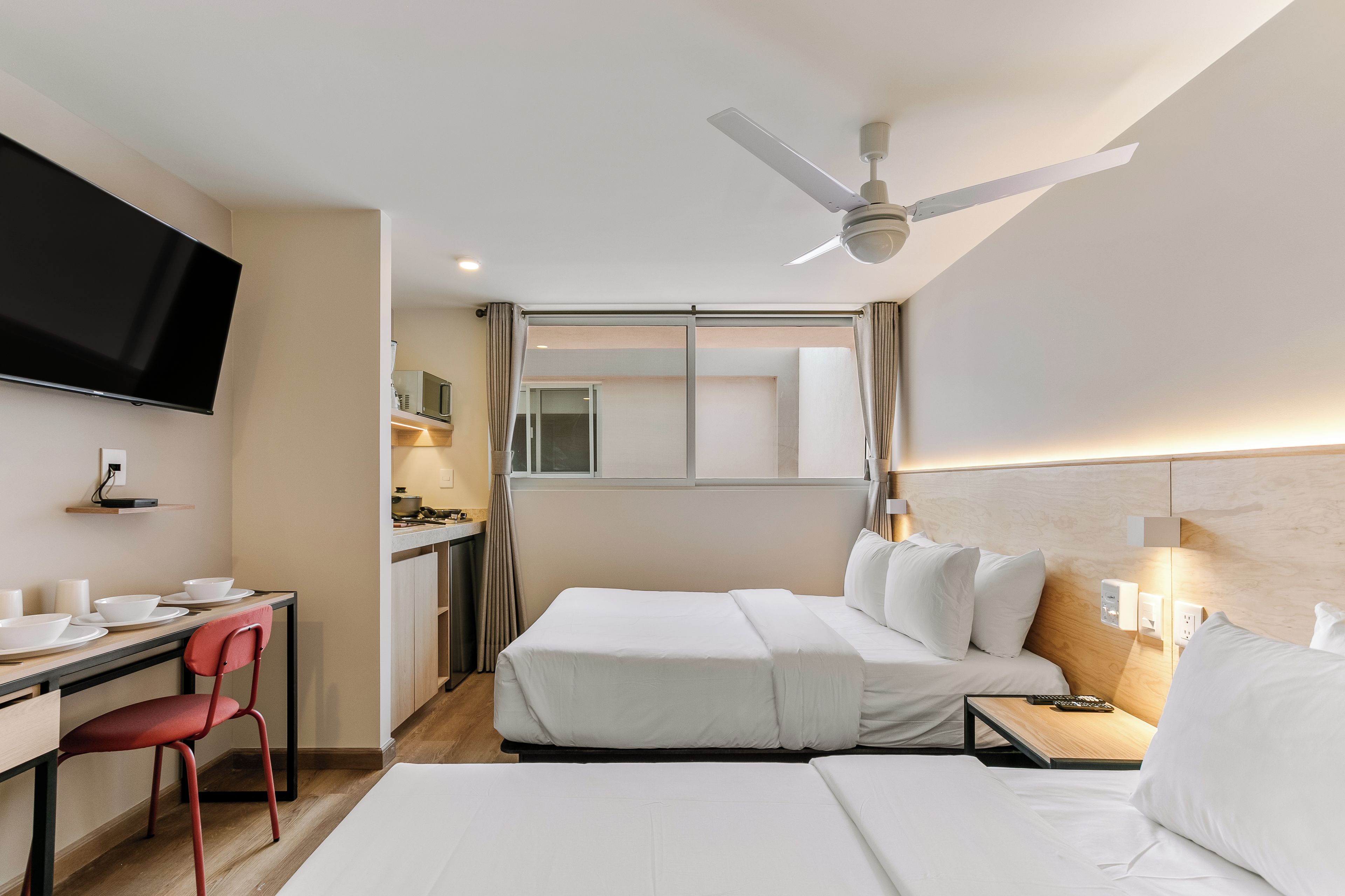 A hotel room with a bed, a desk with a chair, a television, and a ceiling fan.