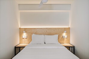 Ein modernes Hotelzimmer mit einem Holzkopfteil, zwei Nachttischen und einem Bett mit weißen Leinentüchern.