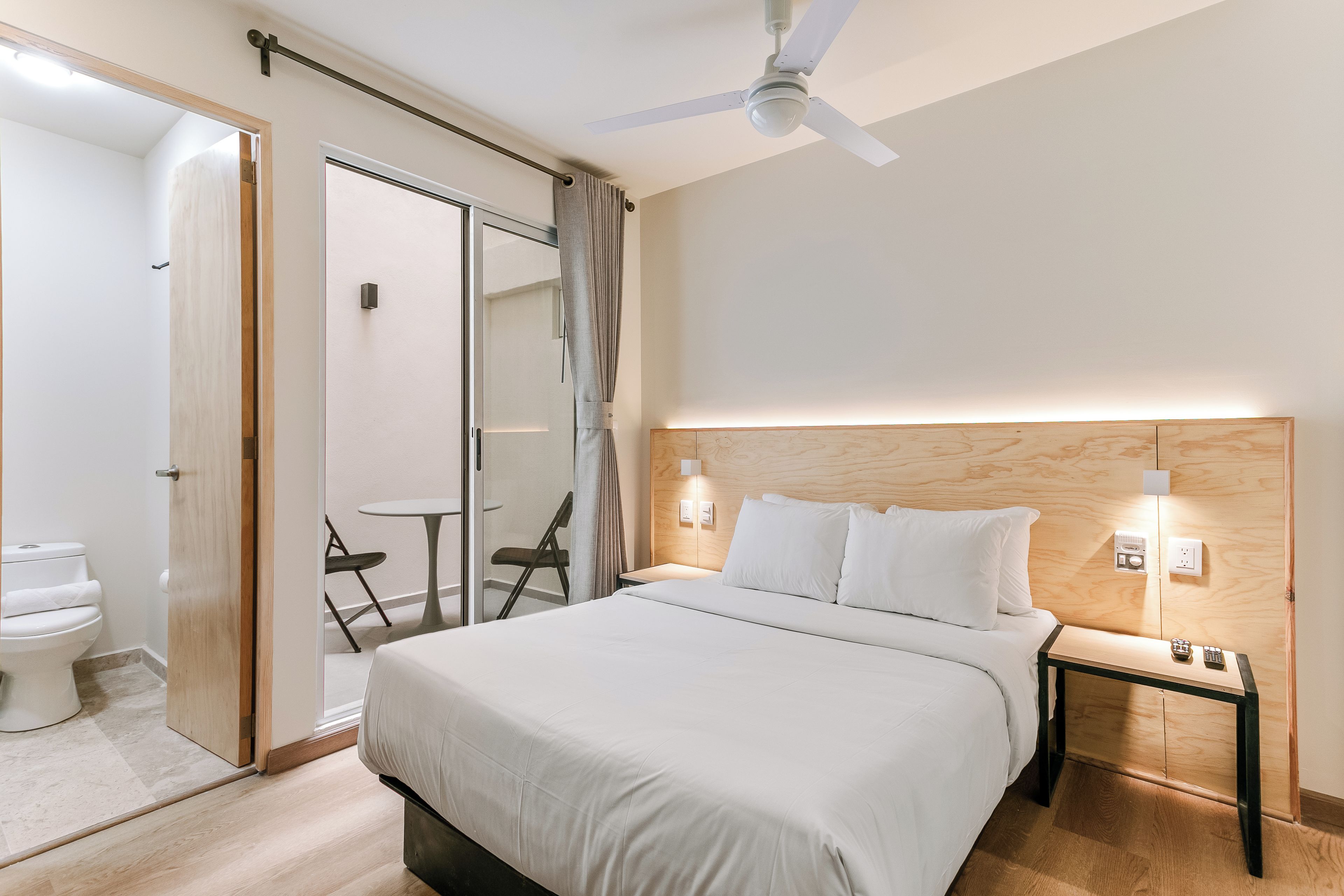 Una habitación de hotel con cama, mesita de noche y ventilador de techo.