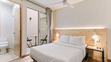 Una habitación de hotel con cama, mesita de noche y ventilador de techo.