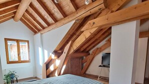 Un dormitorio con techo estilo loft, una cama con colcha escocesa, una ventana con persianas y un radiador.