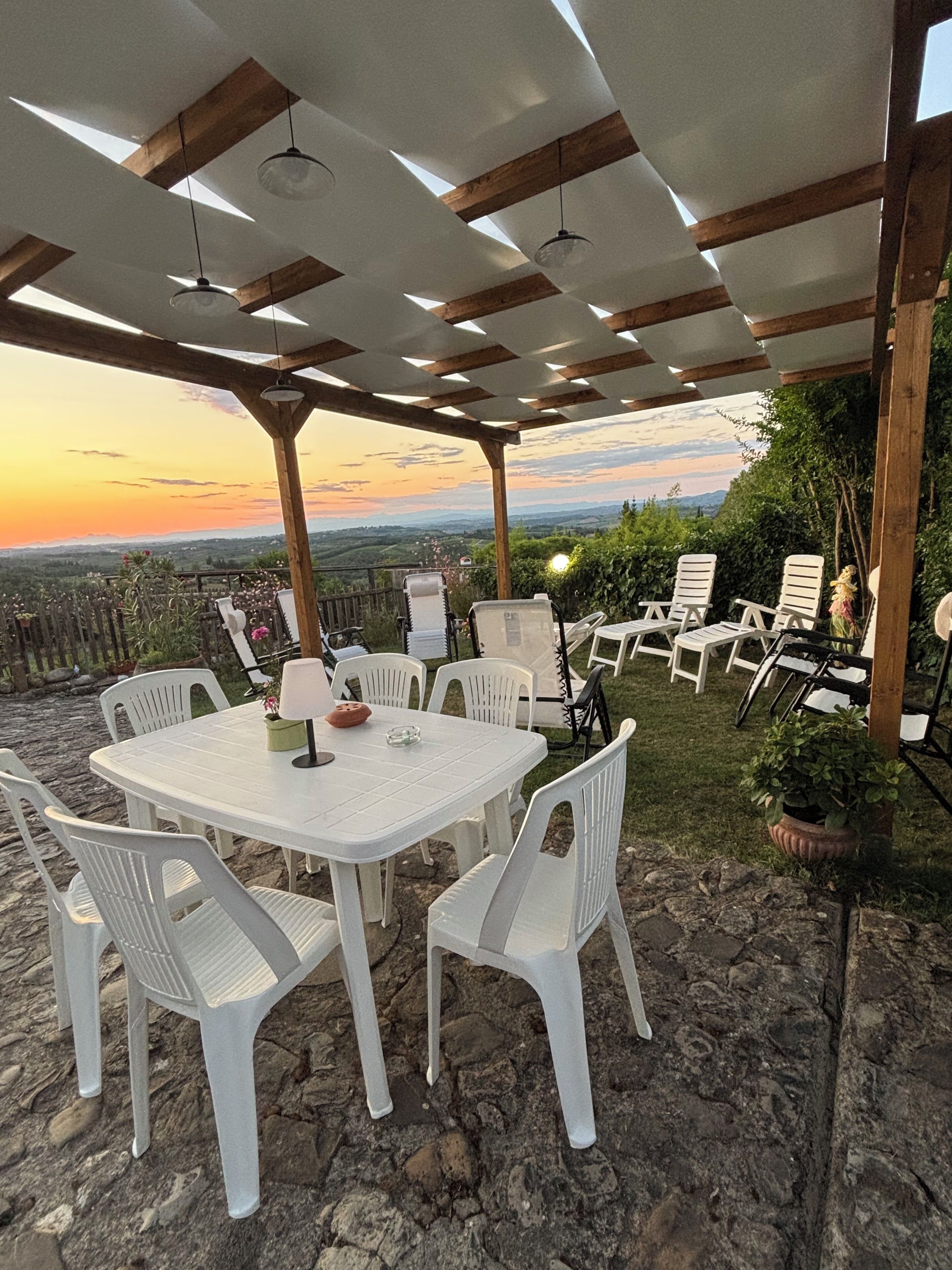 Une terrasse extérieure avec une table ronde et des chaises blanches, entourée d’un sol en pierre et d’une pergola en bois.