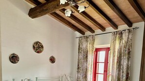 Une chambre avec deux lits simples, une table de chevet, une lampe et une fenêtre agrémentée de rideaux à motifs floraux.