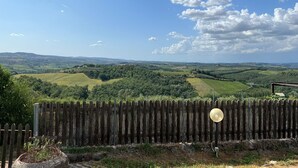 Un paysage rural avec des collines douces, une clôture en bois et un ciel bleu dégagé.