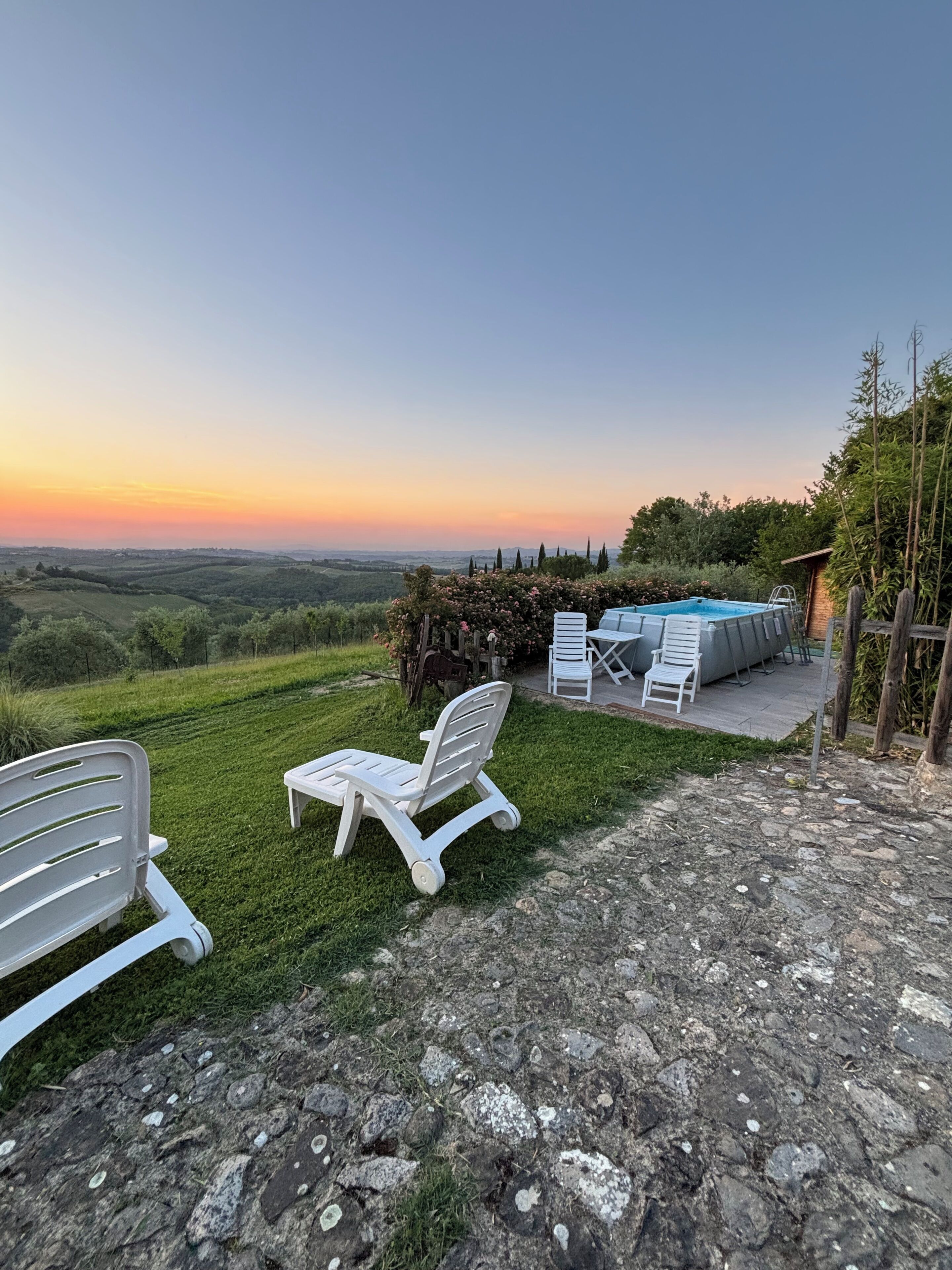 A patio with white chairs and a pool, overlooking a hilly landscape.