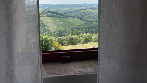 Une fenêtre donnant sur des collines ondoyantes et un bâtiment situé au loin.