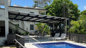 Ein Pool mit Pergola, Liegestühlen und einer überdachten Terrasse.