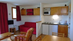 A compact living space with a kitchenette, a dining area with a wooden table and chairs, a red sofa, and a small TV. - 4th floor, view mountain, terrace, balcony, tv, ski locker, 36m², Valfréjus (Valfréjus)