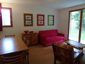 A room with a wooden dining table, a red sofa, and a window with a view of greenery. - 4th floor, view mountain, terrace, balcony, tv, ski locker, 36m², Valfréjus (Valfréjus)