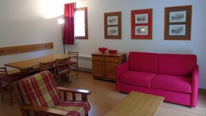 A living room with a wooden dining table, a red sofa, a plaid armchair, and a wooden cabinet. - 4th floor, view mountain, terrace, balcony, tv, ski locker, 36m², Valfréjus (Valfréjus)