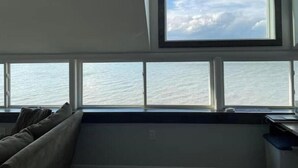 A room with a large window overlooking the sea, a built-in bench, and a desk with a chair. - Lakefront Home Huron/Vermillion Amazing View (Vermilion)