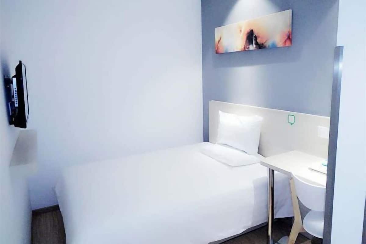 A hotel room with a bed, a bedside table, a TV mounted on the wall, and a painting above the bed.