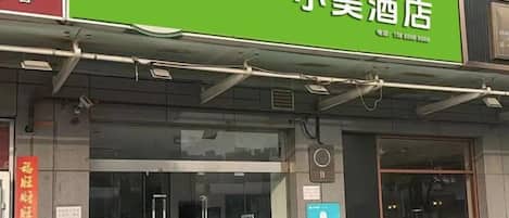 A hotel with a green signboard, a reception desk, and a visible entrance.