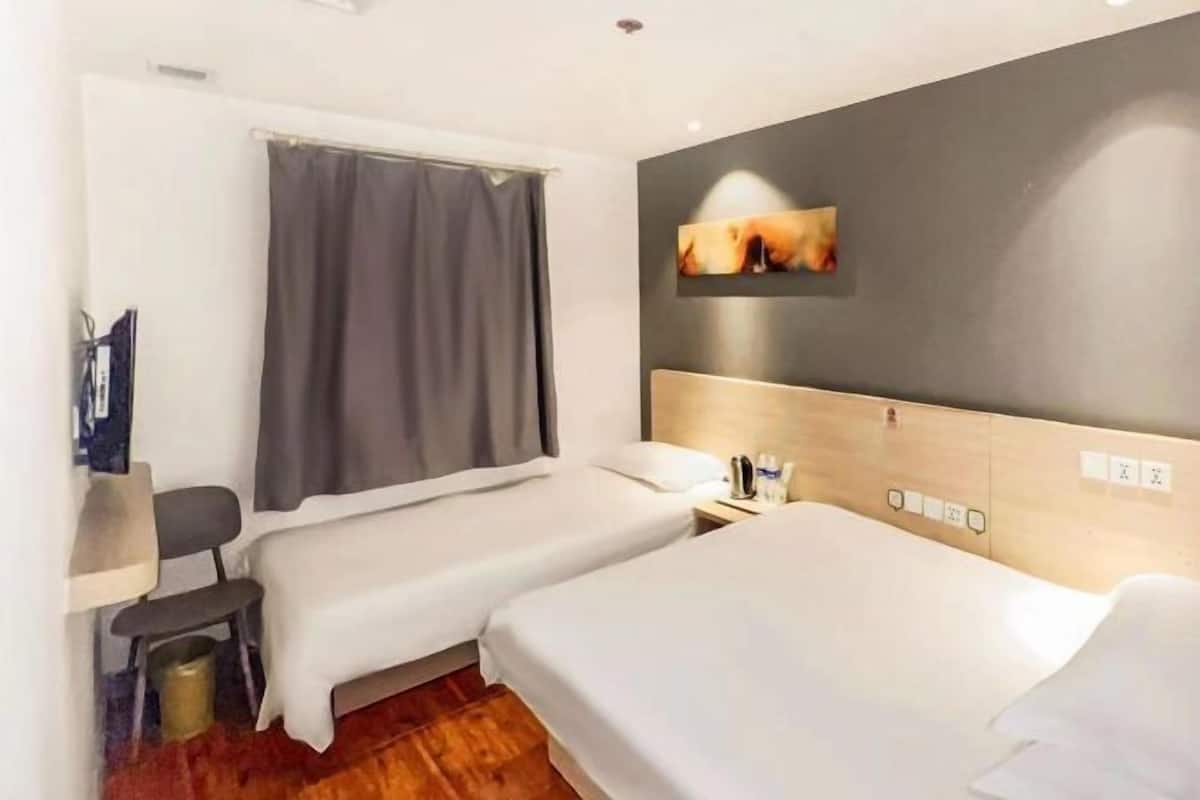 A hotel room with two single beds, a desk, a chair, a small trash bin, and a wall-mounted TV.