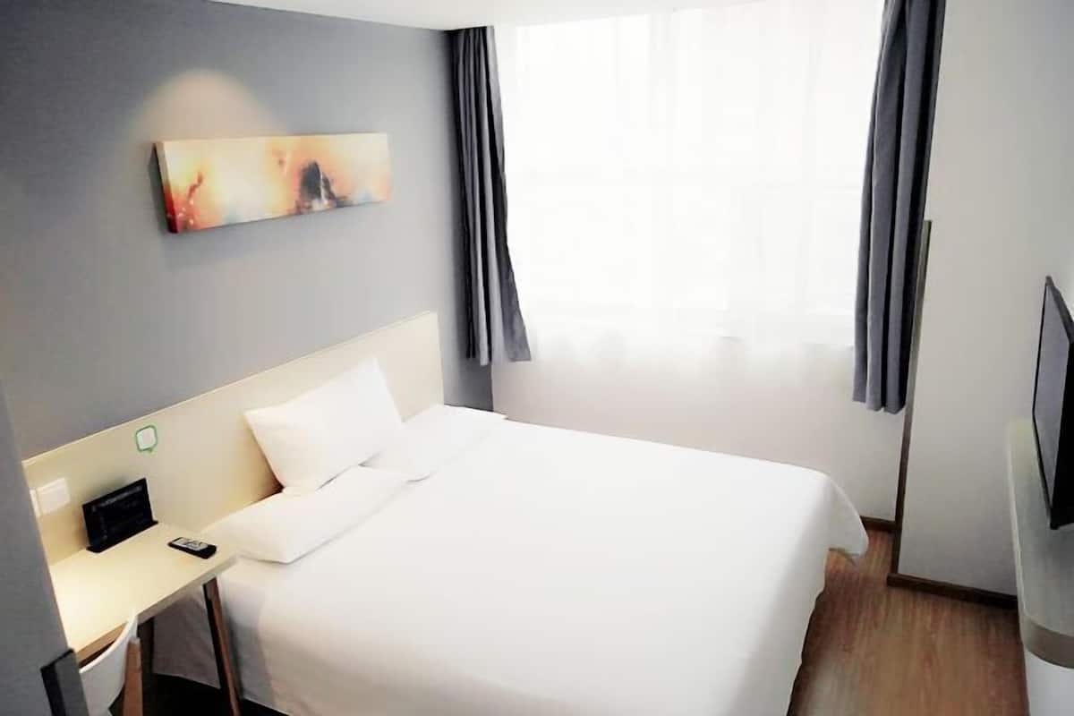 A hotel room with a large bed, a desk with a chair, a flat-screen TV, and a painting on the wall.