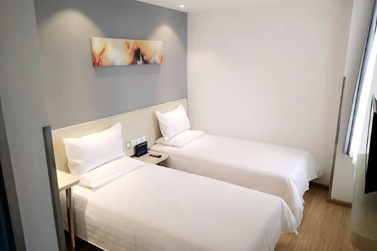 A hotel room with two single beds, a nightstand, a painting on the wall, and a window.