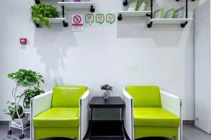 A waiting area with two green chairs, a small table, and wall-mounted shelves with plants and signs. - Xiaomei Hotel (Beijing Universal Studios Tuqiao Subway Station) (Beijing)