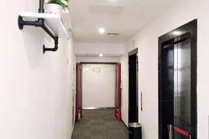 A hallway with a white wall, a black door, a red door, and a trash bin. - Xiaomei Hotel (Beijing Universal Studios Tuqiao Subway Station) (Beijing)