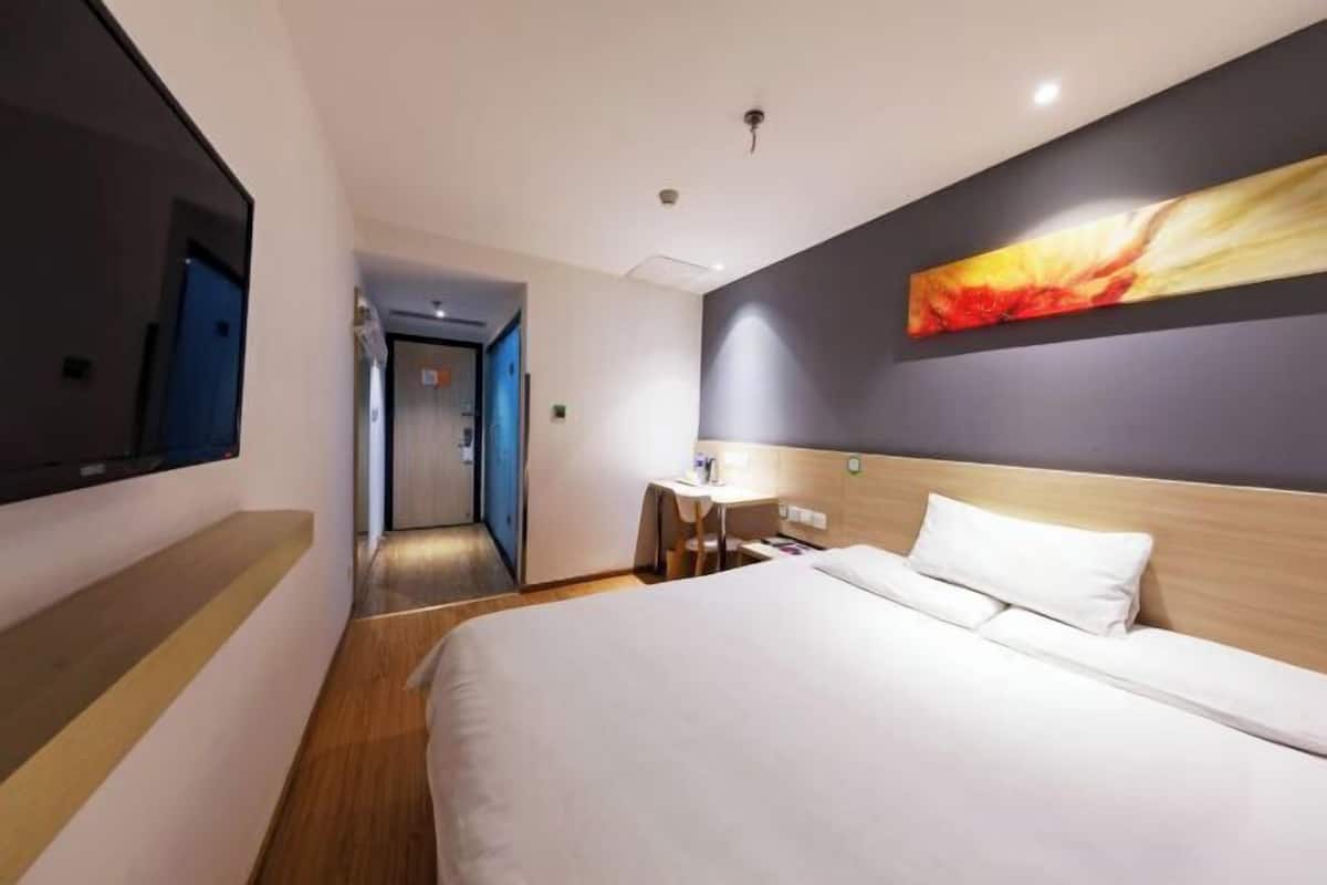 A hotel room with a bed, a desk, a chair, a TV, and a painting on the wall.