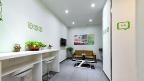 A reception area with a white desk, a brown sofa, and a TV on the wall. - Xiaomei Hotel (Beijing Universal Studios Tuqiao Subway Station) (Beijing)