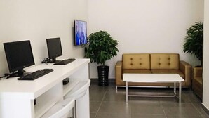 A reception area with two computer monitors, a keyboard, a white table, a beige sofa, and two potted plants. - Xiaomei Hotel (Beijing Universal Studios Tuqiao Subway Station) (Beijing)