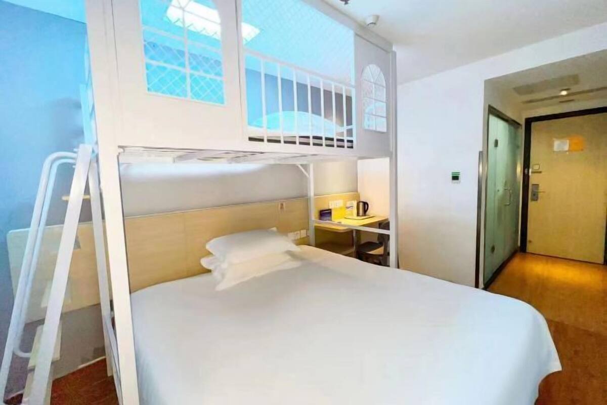 A bunk bed room with a ladder, a desk with a lamp, and a door.