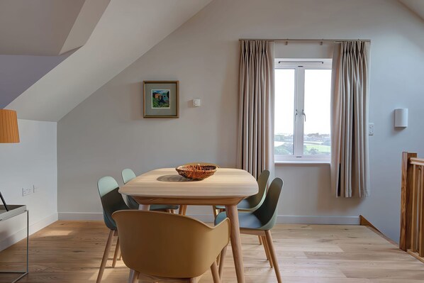 A dining area with a table and chairs, a window with curtains, and a framed picture on the wall.
