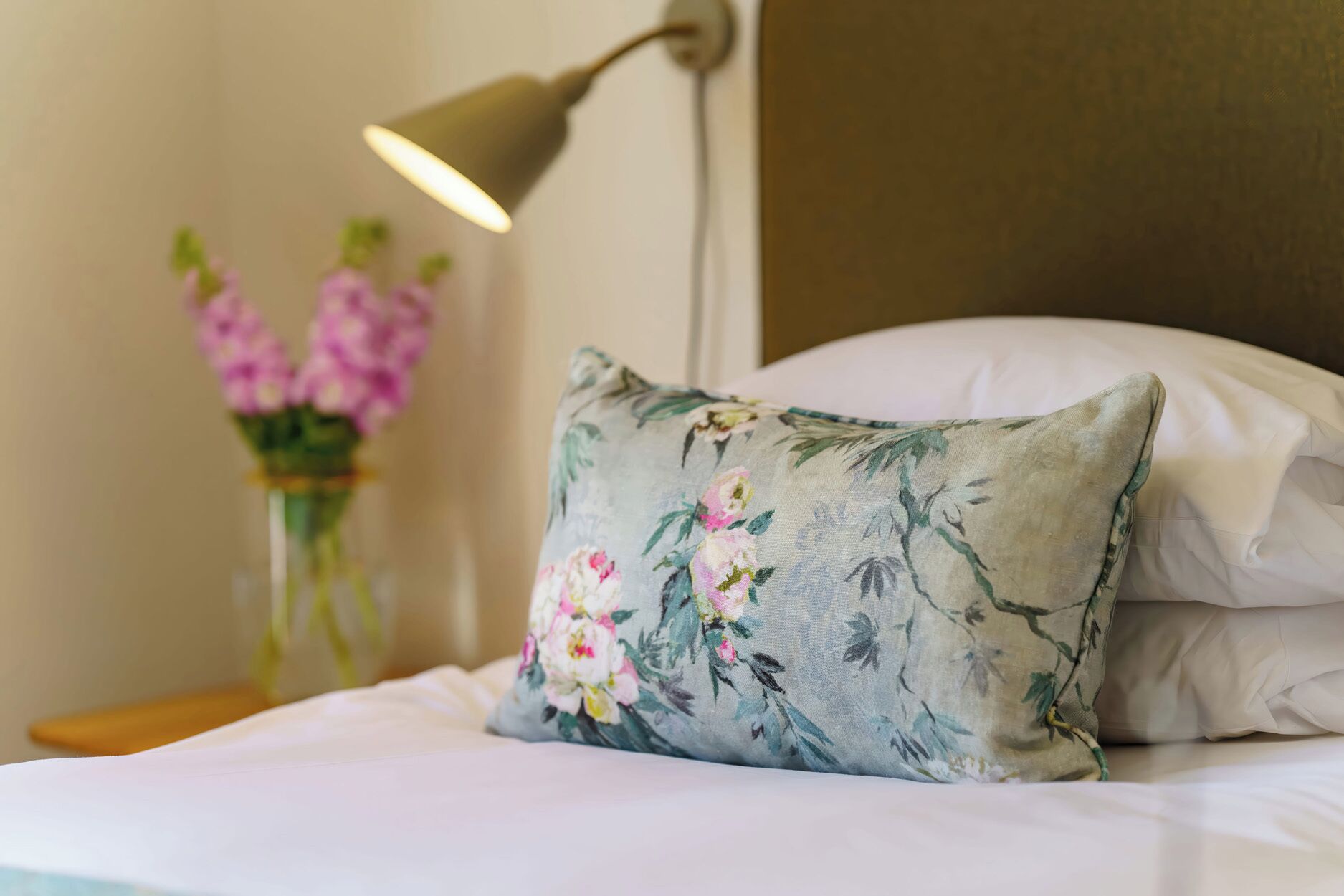 Een keurig opgemaakt bed met een bloemenkussen en een bedlampje.