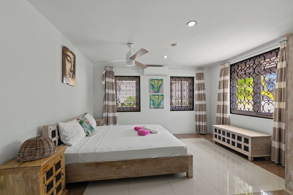 Une chambre à coucher avec un lit, un ventilateur de plafond, un banc et des œuvres d’art accrochées aux murs.