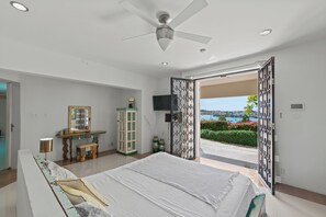 Une chambre avec un lit, un ventilateur de plafond, une télévision, un bureau avec un miroir et une vue sur l’extérieur.