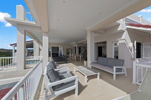 Un espace extérieur abrité, aménagé avec du mobilier blanc, comprenant des canapés et des fauteuils, une piscine et un coin repas.