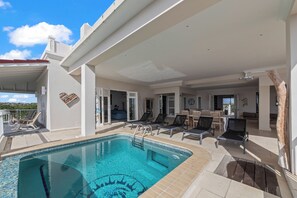 Un espace piscine avec des chaises longues, une piscine avec un escalier et un patio couvert.
