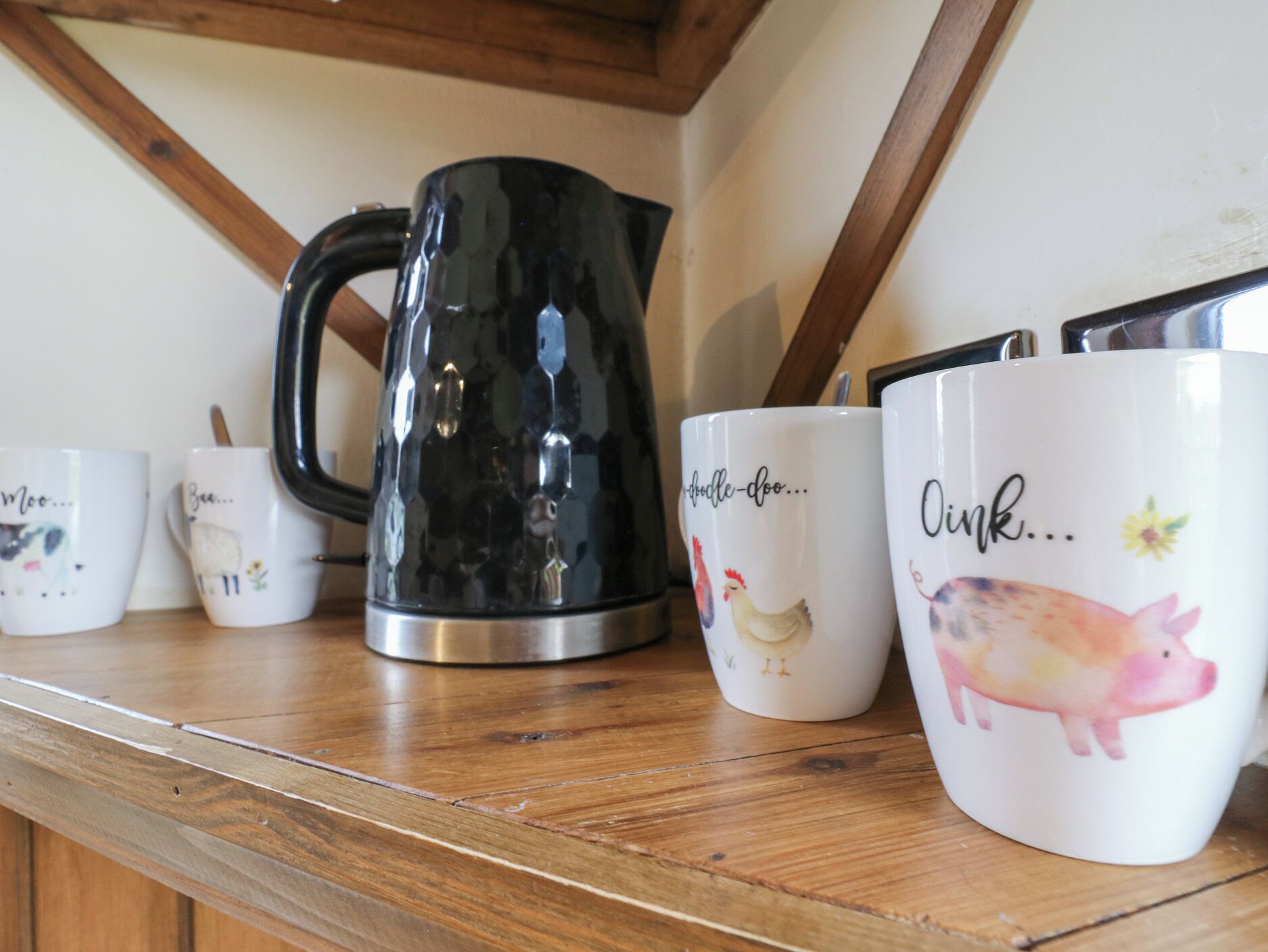 A wooden shelf with a black kettle and white mugs with animal prints and text.